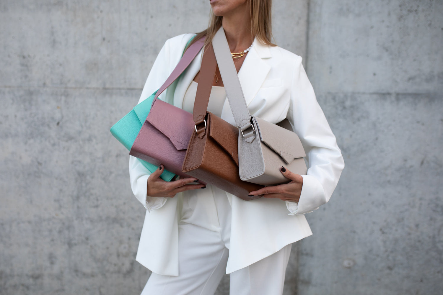 Person holding multiple colorful handbags against a plain background